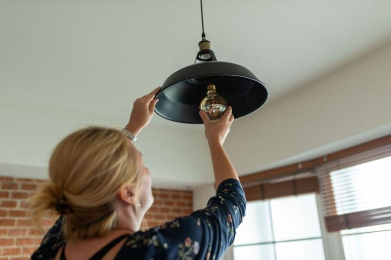 A woman with blonde hair screwing a lightbulb into an overhead light