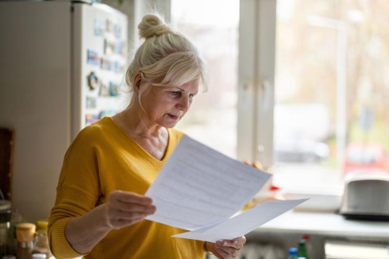 A middle-aged woman in a mustard yellow jumper looking at financial documents