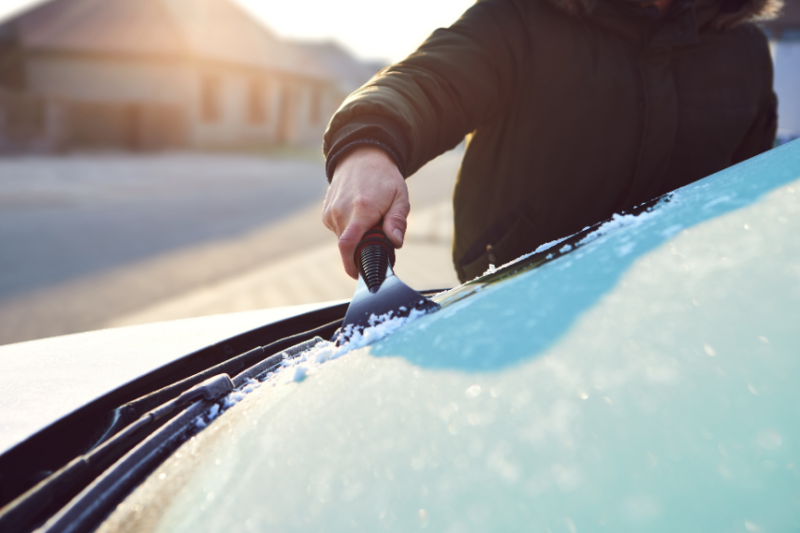 person scraping frost off car windscreen