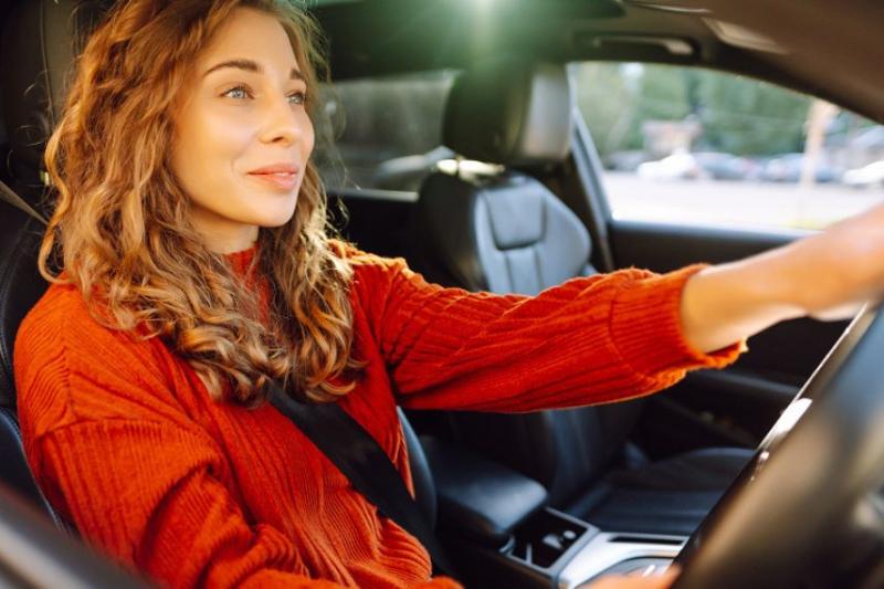 A woman with curly hair in a red jumper driving a car