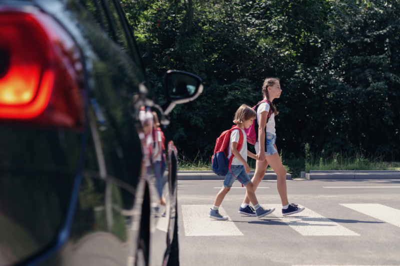 Two children crossing a pedestrian crossing with a car coming in front