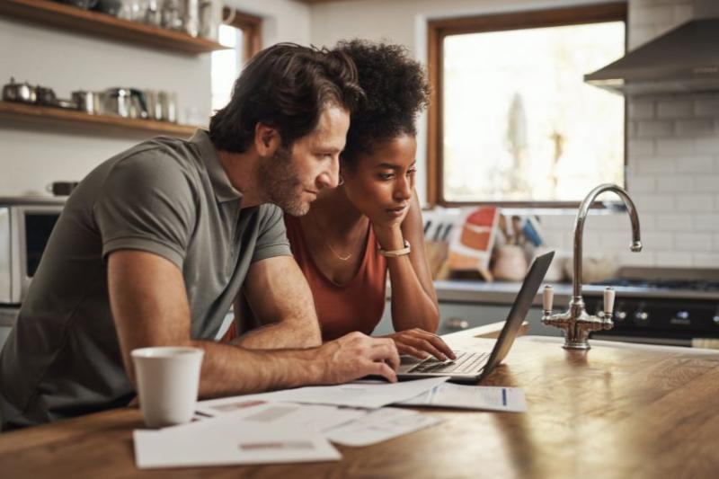 A couple looking at laptops and financial documents on their kitchen island