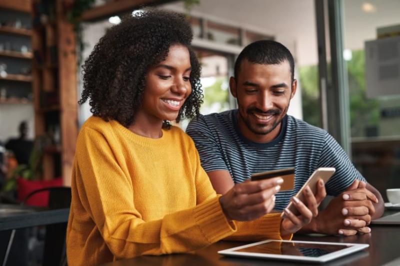 A couple at a table using their credit card to buy something on a phone