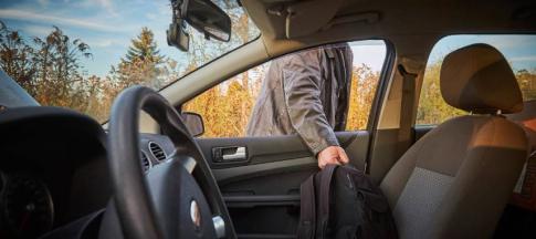 Image of a man stealing a bag from a parked car. 