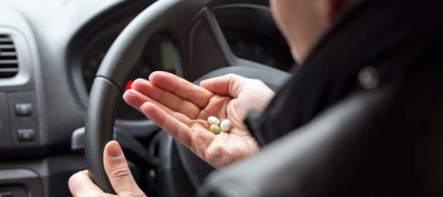 Image of a man looking at pills before driving.