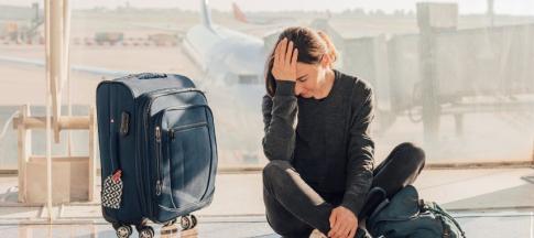 Woman with her head in her hands at airport with suitcase beside her