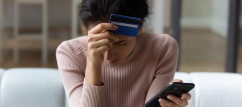 Woman with head in hands holding a credit card and her phone