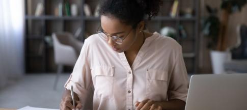 A young woman sat at a table budgeting with her laptop and calculator