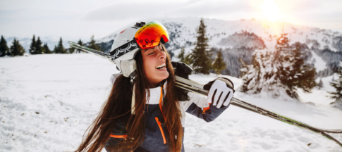 A woman holding her skis over her shoulder on a ski slope and smiling