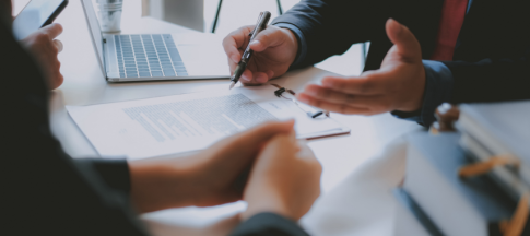 Shot of a desk with laptop and contract and two people speaking over it