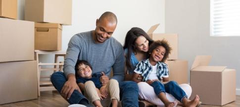 Family of four sitting on floor of house surrounded by boxes
