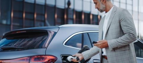 A man in a grey suit charging his EV