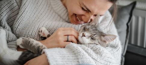 Woman in grey jumper cuddling a grey cat