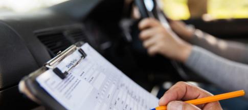 A view of a driving test clipboard with someone's hands on the steering wheel in the background
