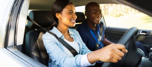 Two people in a car, one person with a lanyard teaching them how to drive
