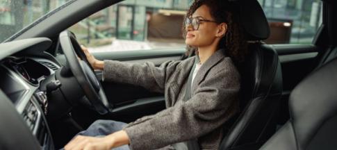Woman in grey coat and glasses driving