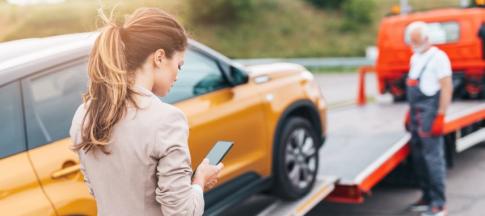 Woman on the phone standing in front of orange car being towed