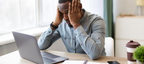 A man at a laptop with his head in his hands looking stressed