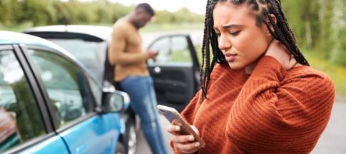 A woman looking stressed on the phone in front of a car accident