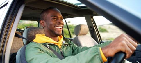 A young man in a green coat smiling and driving a car