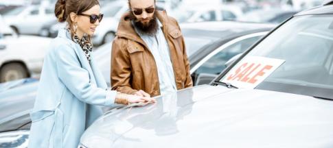 A young couple looking at a car that has a 'sale' sign on it 