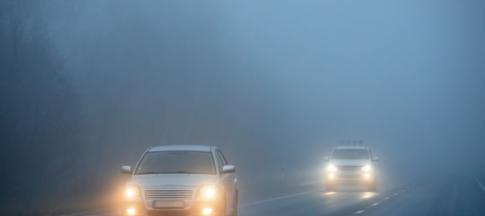 Two cars driving on a road through heavy fog