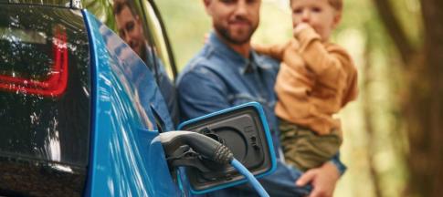 A blue EV being charged with man and son in the background