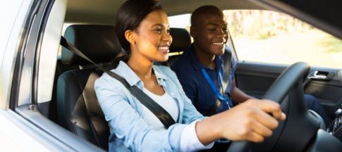 A young woman in a blue shirt, driving in a car with a driving instructor 