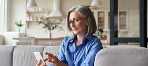 A mature woman sitting on a grey sofa in her house on the phone