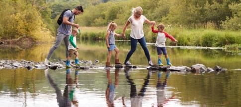 A mother and father with three young children crossing stepping stones across a river in the Lake District, UK