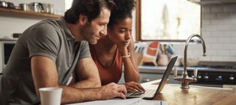 A couple standing a kitchen island looking at a laptop with some paper spread in front of them