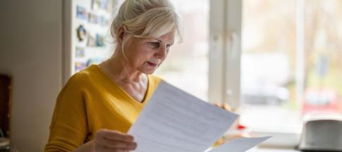 A middle-aged woman in a mustard yellow jumper looking at financial documents