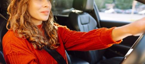 A woman with curly hair in a red jumper driving a car