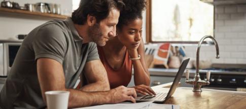 A couple looking at laptops and financial documents on their kitchen island