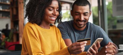 A couple at a table using their credit card to buy something on a phone
