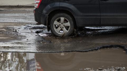 Car driving through water filled pothole
