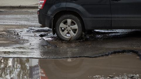 Close up of a wheel on a black car driving through a pothole full of rainwater